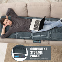 Full-body vibrating massage mat with 10 motors and heat, shown on a sofa with a user relaxing and working on a laptop.