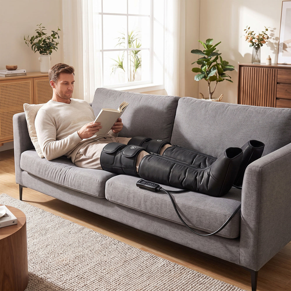 A man relaxing on a grey sofa while using a Costway heated leg compression massager.
