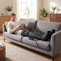 A man relaxing on a grey sofa while using a Costway heated leg compression massager.